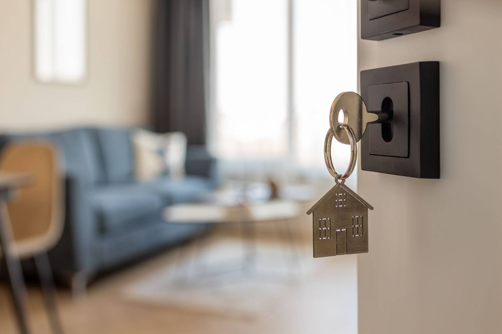 Key with house-shaped keychain in door of modern apartment, symbolising rental property investing for busy professionals