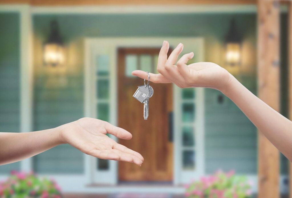 a set of house keys being handed to someone in front of a rental house